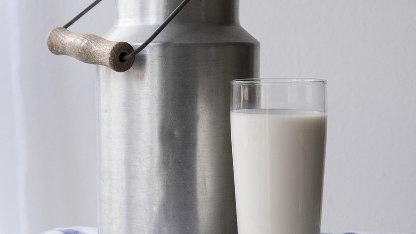 Glas karnemelk naast een traditionele metalen melkkan, passend bij het thema verschil kefir karnemelk