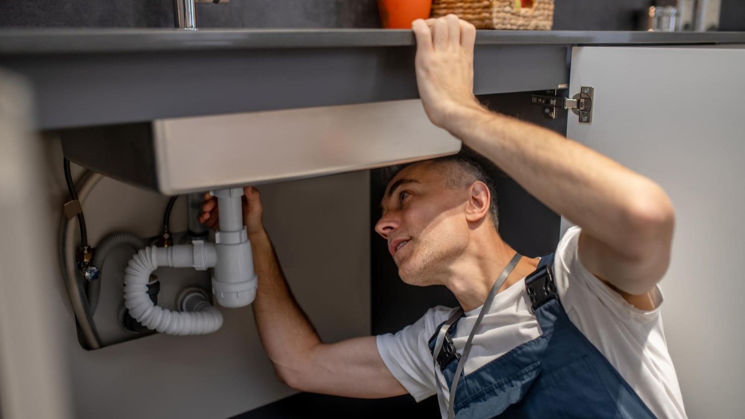 Loodgieter inspecteert sifon onder keukenkastje bij lekkage of verstopping