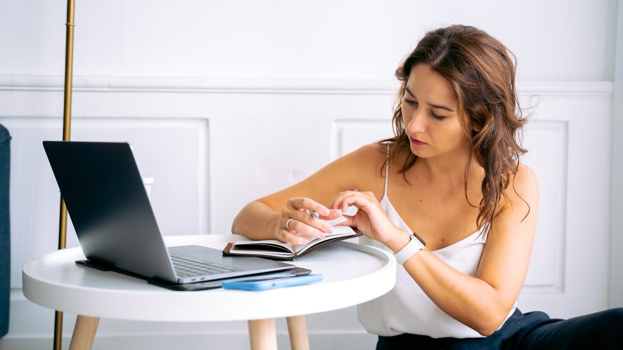 Vrouw werkt thuis als zzp&rsquo;er, maakt aantekeningen naast een open laptop op een ronde tafel