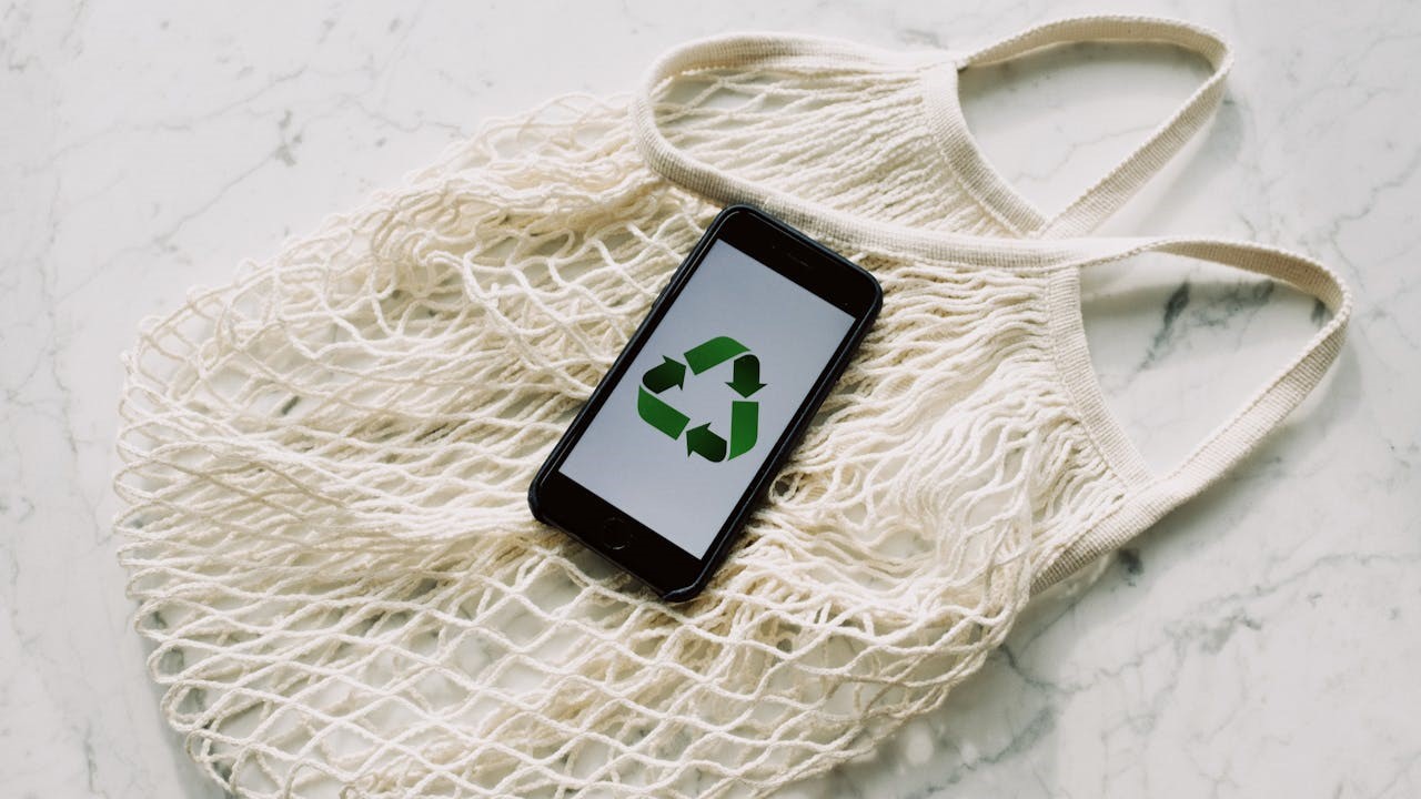 Herbruikbaar netzakje met smartphone die recyclelogo toont, verwijzend naar duurzaam gebruik en bewust afvalbeheer.