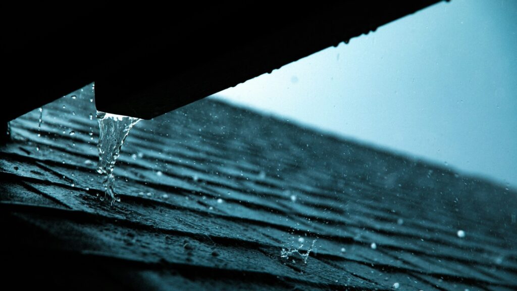 Regenwater stroomt van een dakgoot op dakbedekking, relevant voor keuze tussen EPDM of bitumen