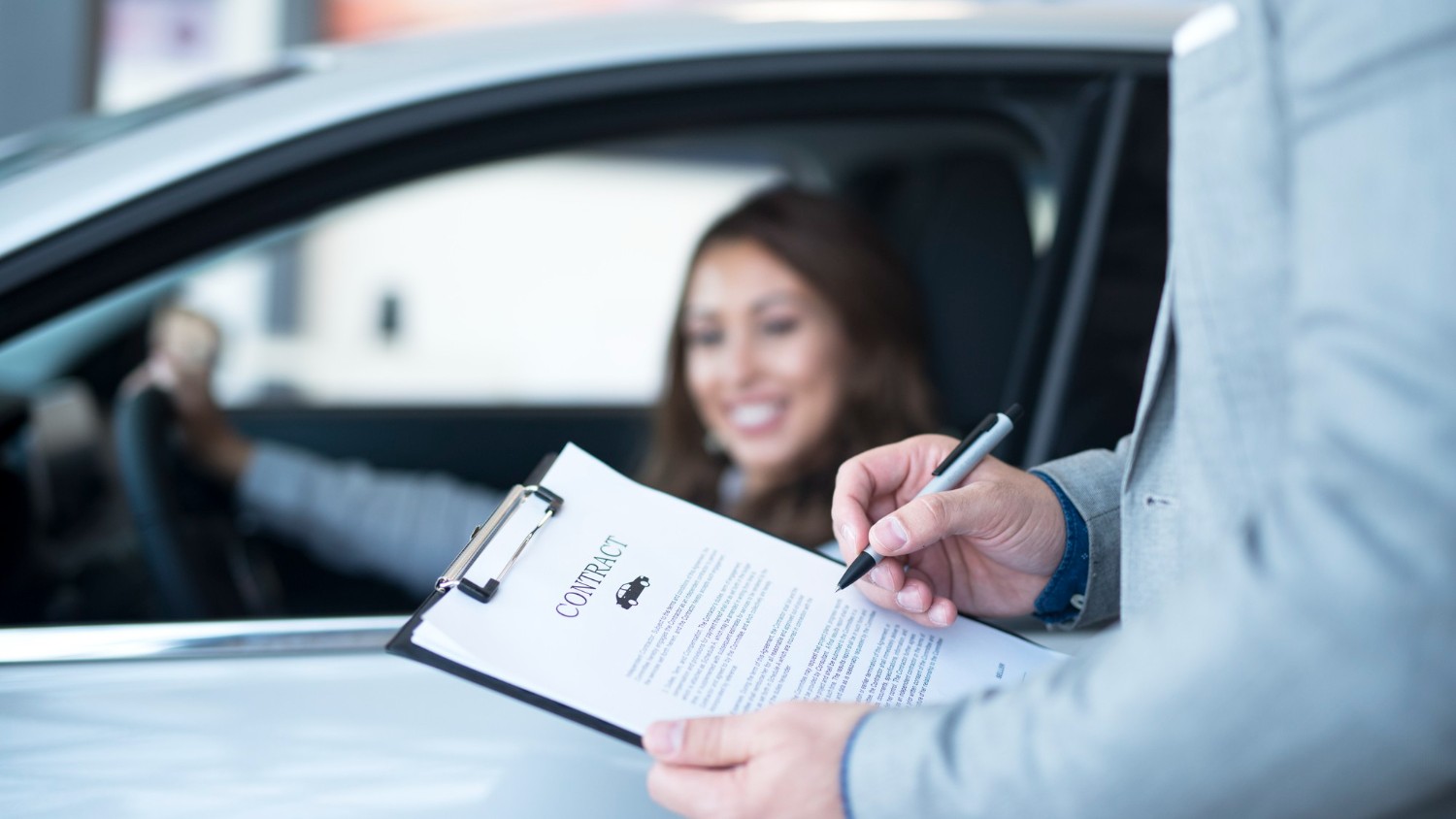 Een handtekening wordt gezet op een leasecontract voor een auto, terwijl een persoon in de auto zit, wat het moment van het ondertekenen van een leaseovereenkomst aangeeft.