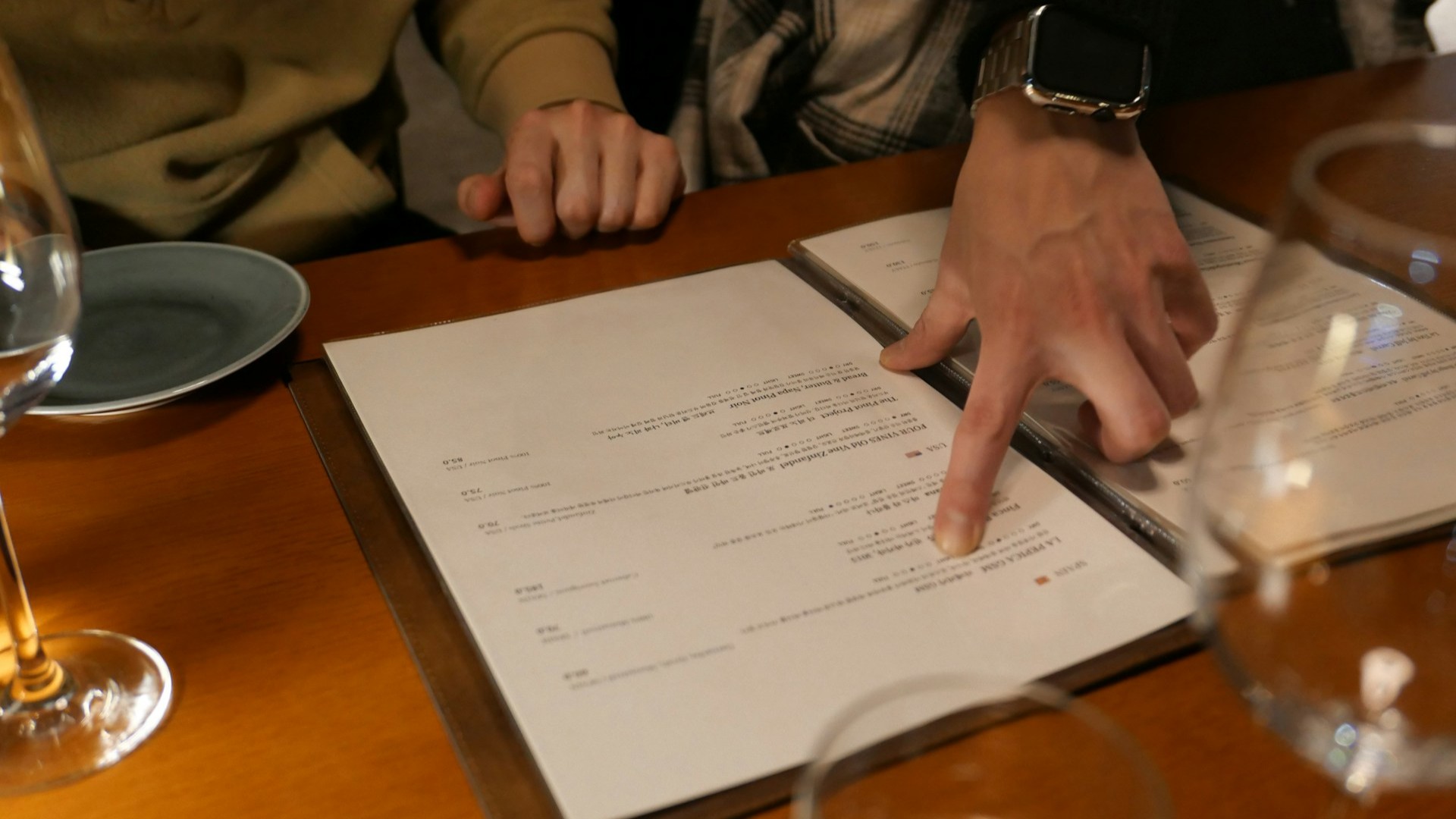 Twee personen bekijken samen een menukaart in een restaurant, waarbij &eacute;&eacute;n persoon een gerecht aanwijst &ndash; verschil menu en &agrave; la carte.