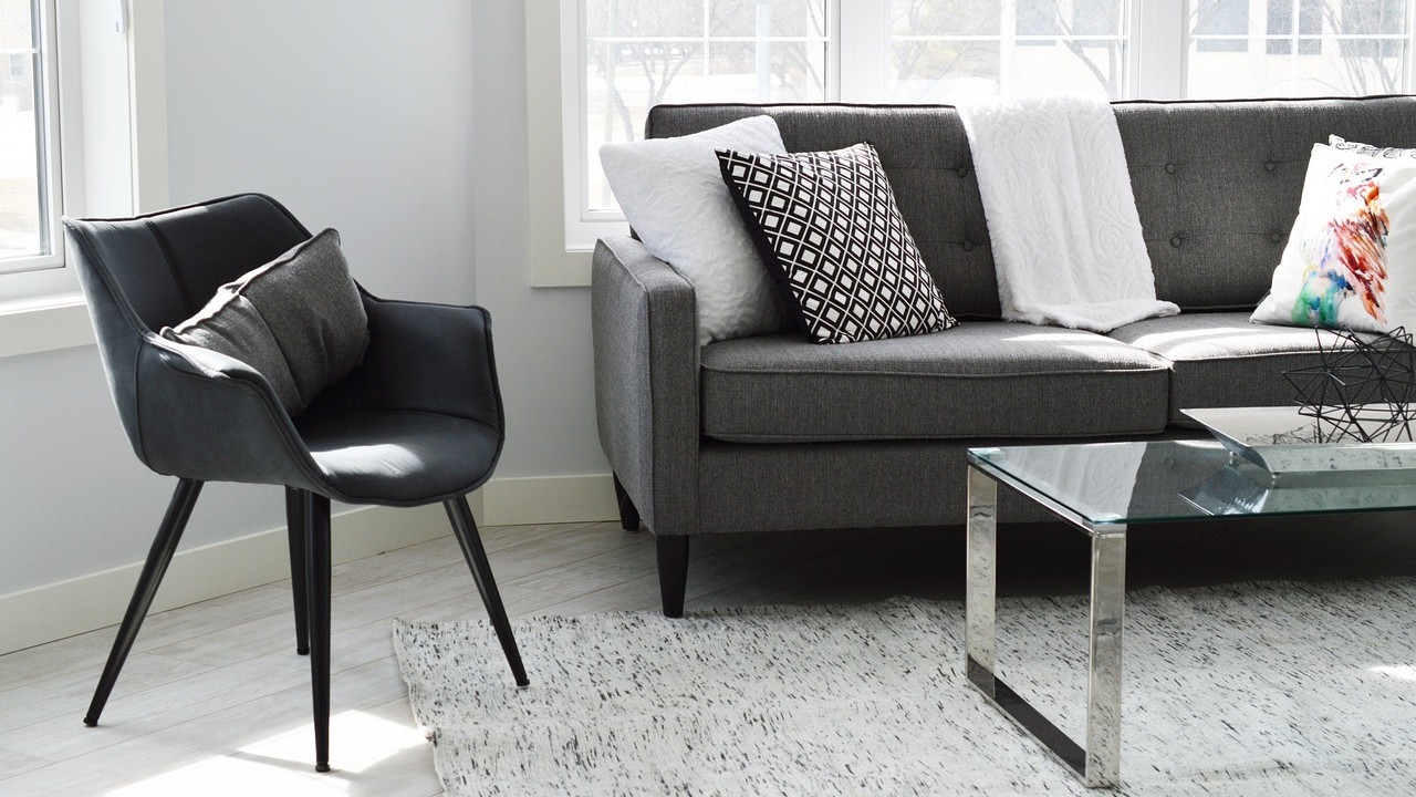Moderne woonkamer met grijze vintage meubels, waaronder een retro bank en zwarte fauteuil, stijlvol gecombineerd met kussens en glas.