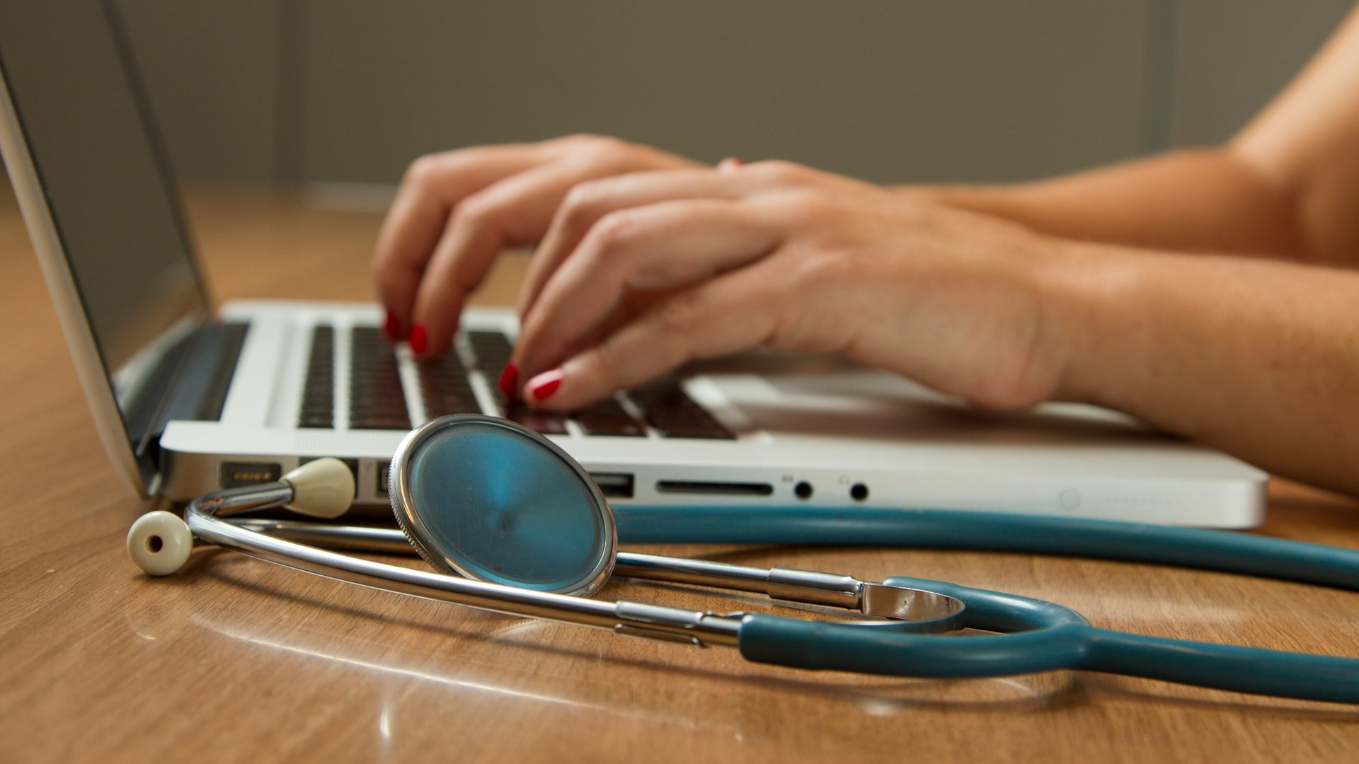 Zorgprofessional typt op laptop naast een stethoscoop, tijdens analyse of verslaglegging van terugval of restklachten.