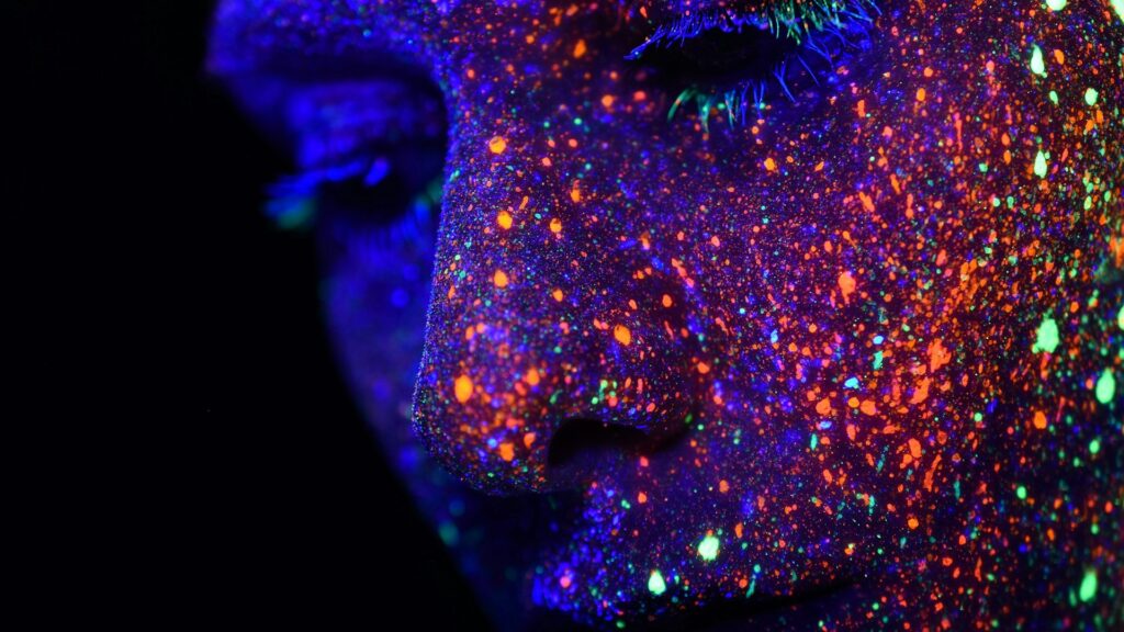 Close-up van gezicht met kleurrijke verfspatten die oplichten onder blacklight UV licht
