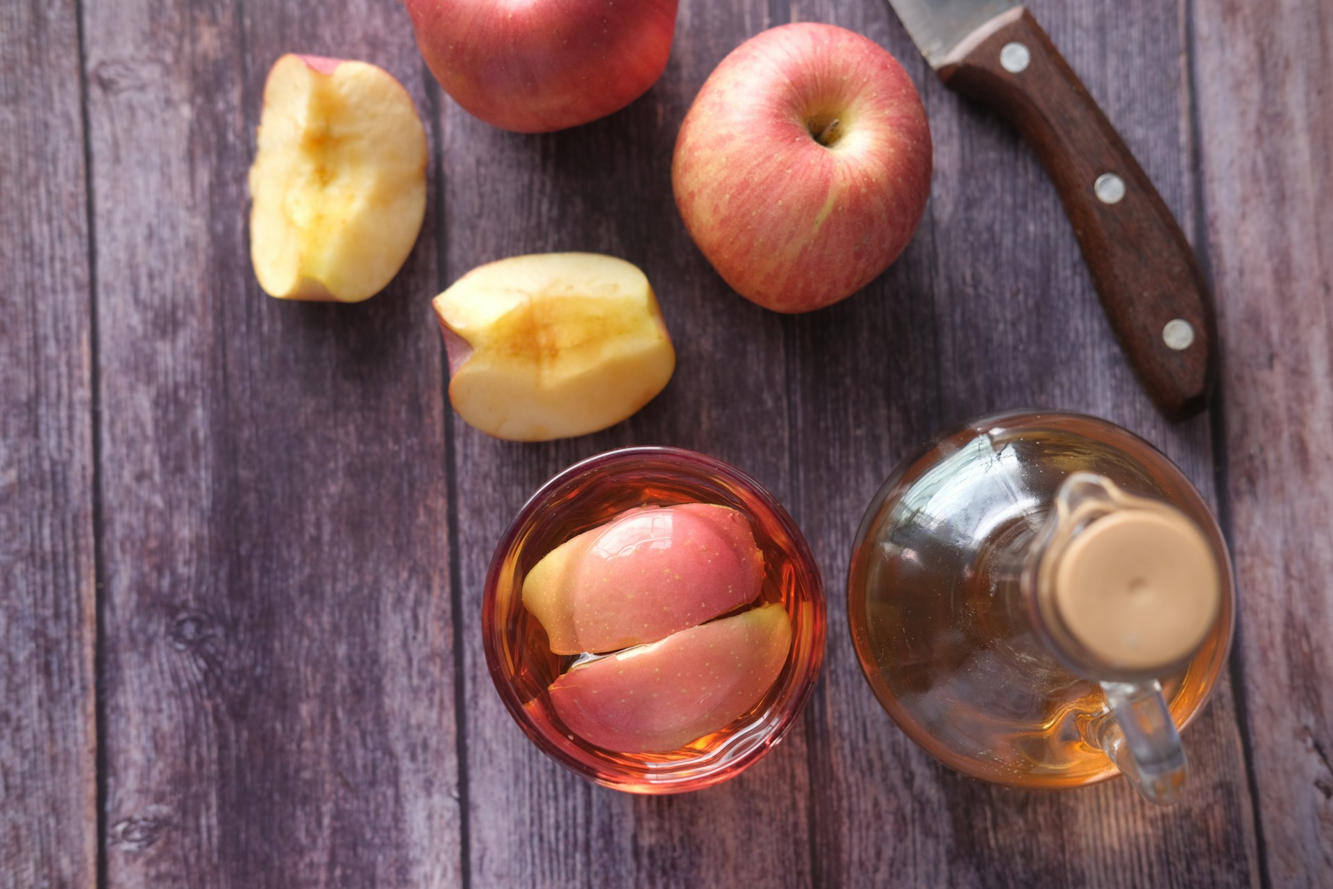 Glas appelazijn met verse appelstukken en fles op houten tafel, focus op natuurlijke azijnsoort.