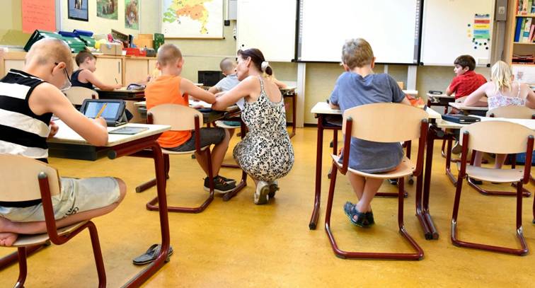 Kinderen werken samen in een klaslokaal met begeleiding van docent &ndash; online leren vs klassikaal leren.