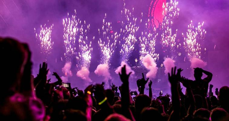 Dansende mensen bij een muziekfestival met lichtshow, rook en vuurwerk op het podium