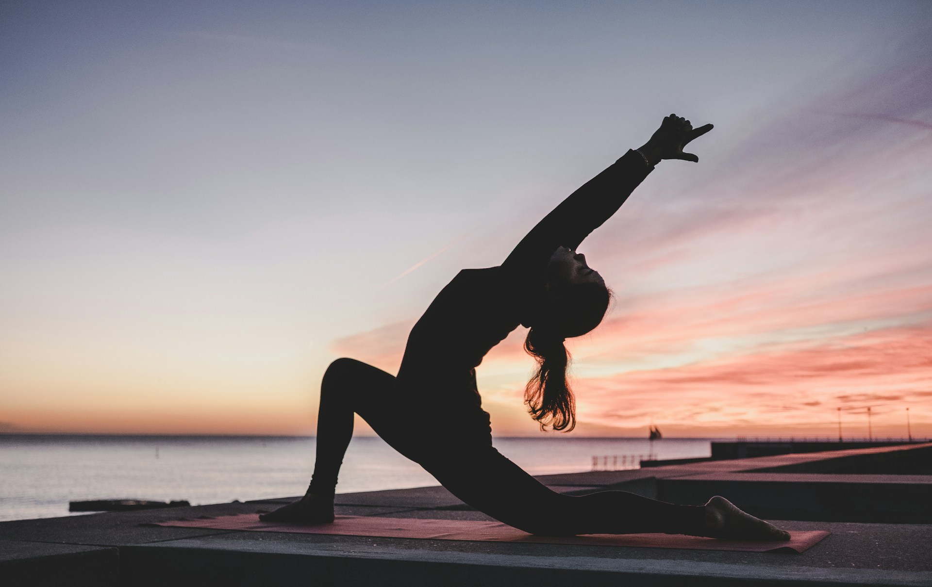 Vrouw doet yoga en pilates stretch in lunge houding bij zonsondergang aan zee